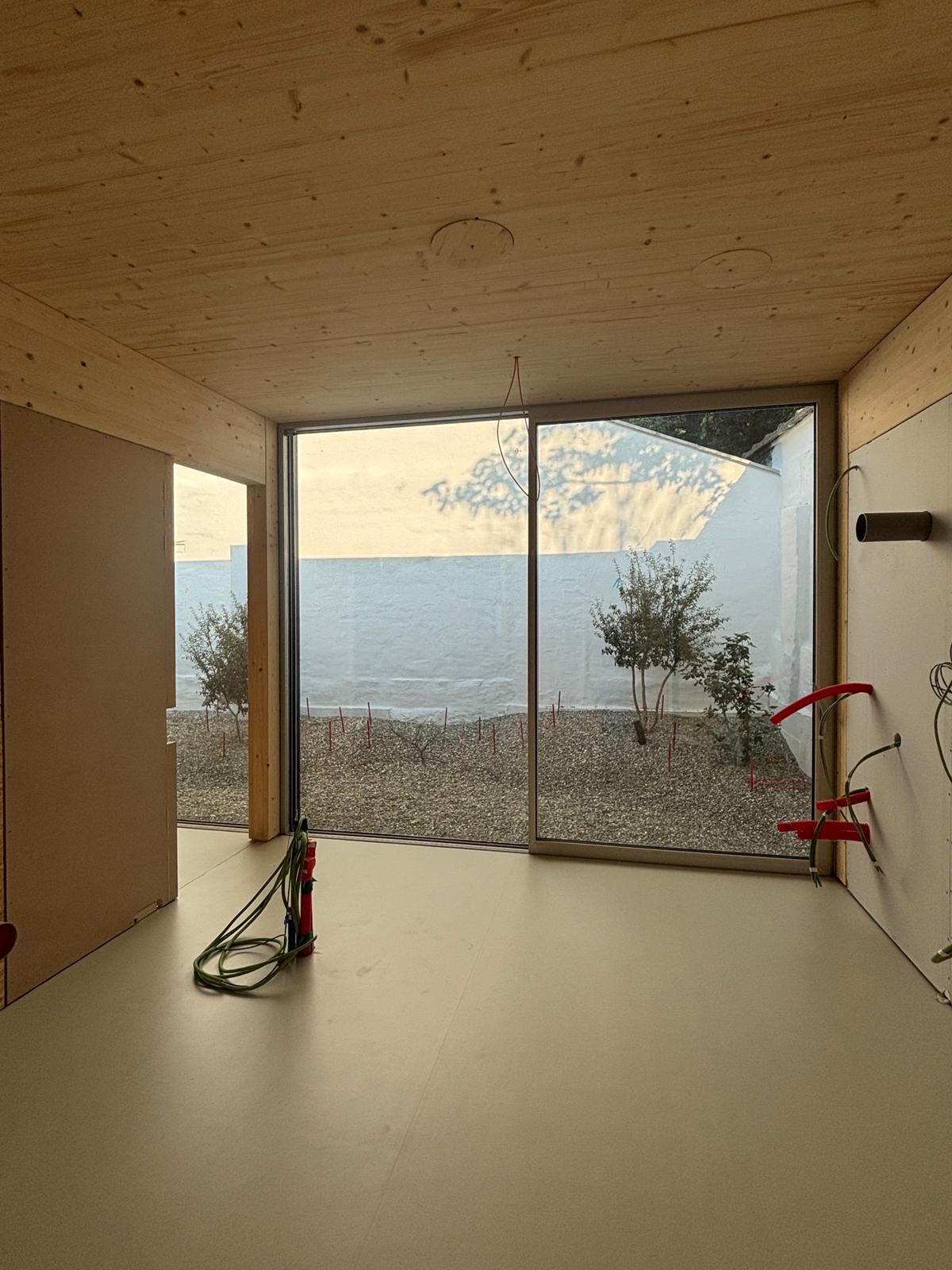 Behandelkamer met groot raam, zicht op de tuin en houten plafond